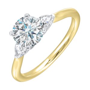 Stunning engagement ring features a round brilliant cut diamond in the center of a three stone setting, adorned on either side by a smaller pear diamond set on the tapered shank.