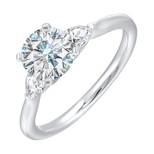 Stunning engagement ring features a round brilliant cut diamond in the center of a three stone setting, adorned on either side by a smaller pear diamond set on the tapered shank.