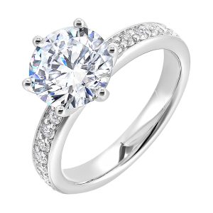 A six prong setting secures round solitare diamond with pave of diamonds in shank is perfect for the classic look.